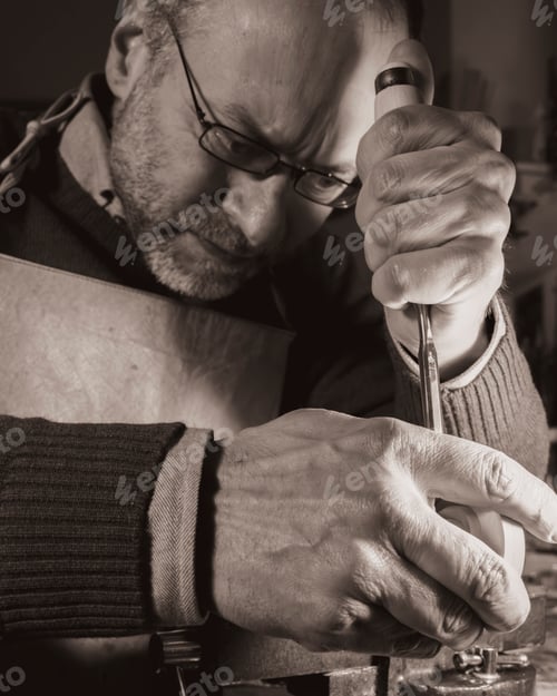 Preview: Violin maker meticulously carves a violin scroll in his workshop, focused on the intricate details