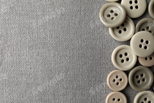 Preview: Many plastic sewing buttons on grey fabric, flat lay. Space for text