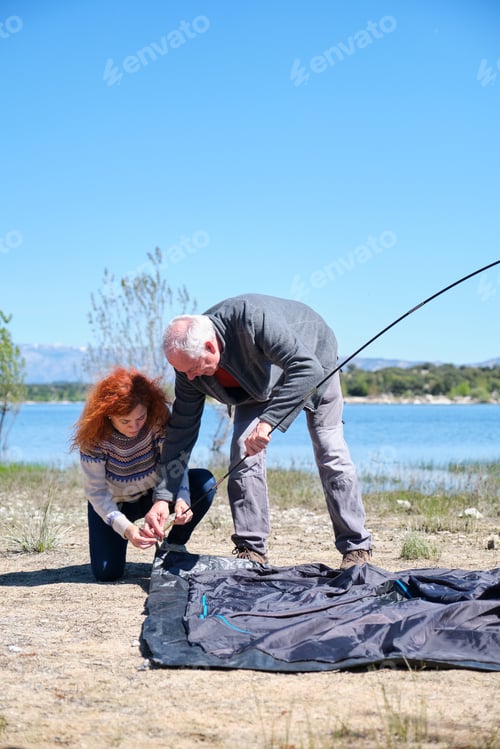 Preview: A man and a woman are setting up a tent by a lake
