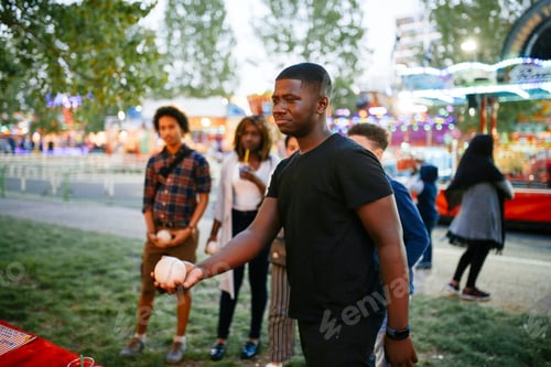 Preview: Group of friends at funfair, boy holding ball, looking towards fairground stall