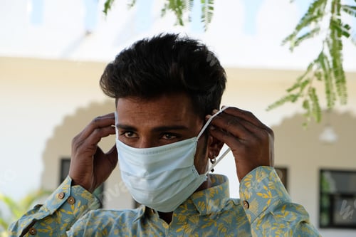 Preview: View of an Indian man wearing a green shirt putting on a protective mask from coronavirus