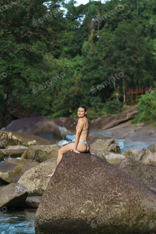 Preview: YYoung and sexy woman stand on rock wearing swimsuit on the beautiful river in the jungle