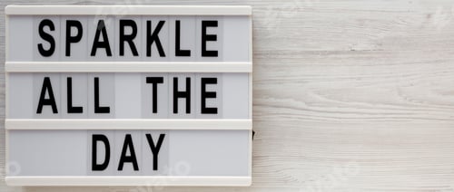 Preview: 'Sparkle all the day' words on a modern board on a white wooden surface, top view.