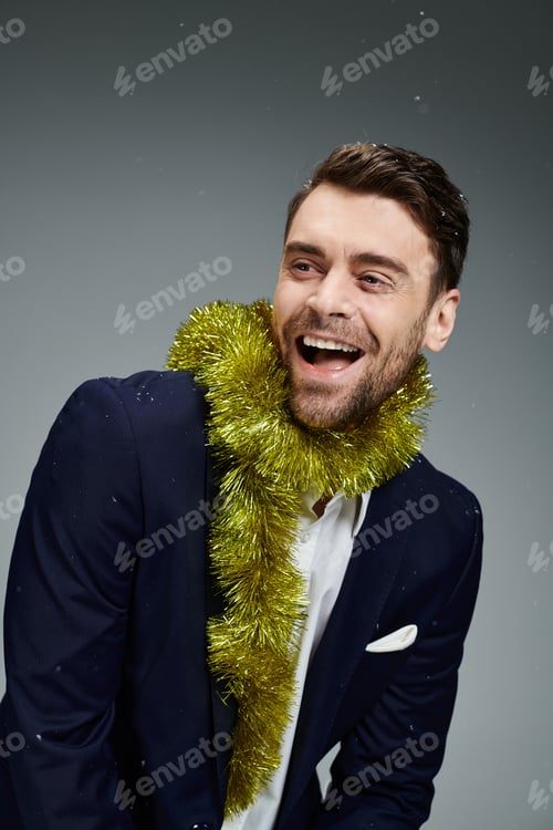 Preview: Joyful young man wearing festive garland smiles brightly against a gray background