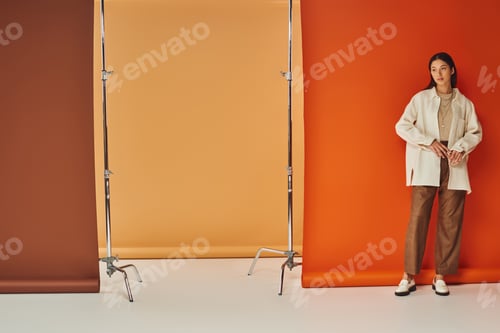 Preview: brunette asian woman in autumn attire standing on multicolored backdrop, leather pants and outerwear