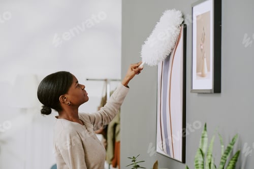 Preview: Black Adult Woman Dusting Wall Art during Home Cleaning Routine