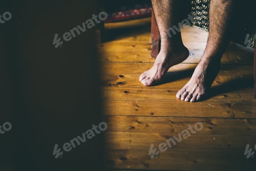 Preview: Bare feet of a man sitting on a chair inside a wooden hut.