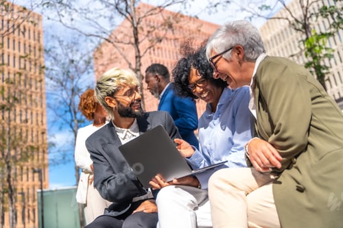 Preview: Happy business team using laptop sitting outdoors in a bench