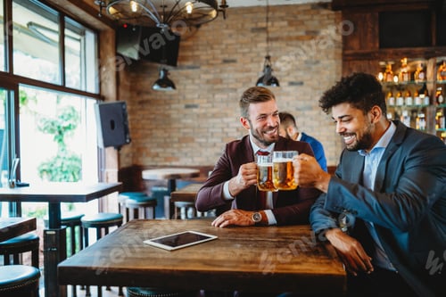 Preview: Happy young businessmen drinking beer and talking at pub after work