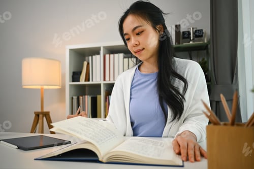 Preview: Charming asian fe male student reading book, preparing for exam or, doing homework in living room