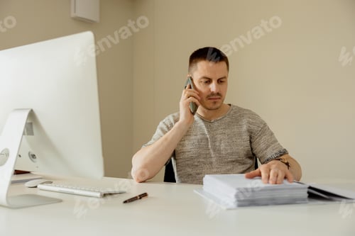 Preview: Young caucasian man sitting at his desk in office, working with computer and communicating