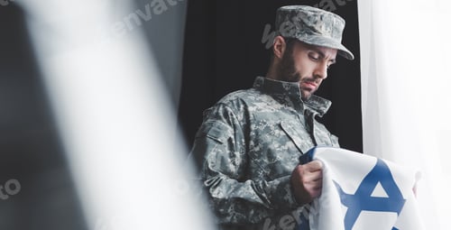Preview: selective focus of pensive military man in uniform holding israel national flag while standing by