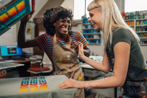 Preview: Interracial print shop workers laughing and silkscreen printing at shop