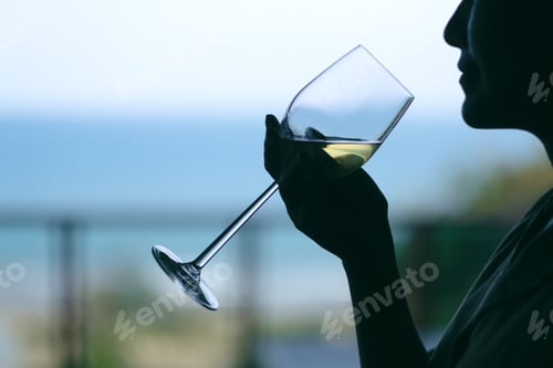 Preview: Silhouette image of a woman holding a wine glass to drink with blurred sea background