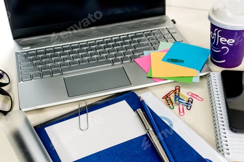 Preview: Closeup of a messy desk with a laptop, notepads, and notes on it in the office