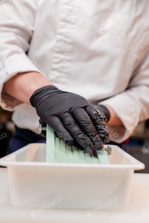 Preview: close-up of the hands of a chef in the kitchen in white jacket grating beets on the table