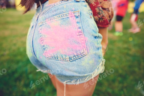 Preview: Cropped view of young woman's denim shorts with pink chalk handprint on buttock at festival