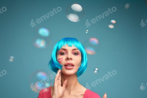 Preview: Beautiful young woman with blue wig and bright make-up in soap bubbles. Fashion model girl with