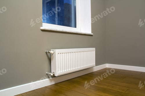 Preview: White metal heating radiator mounted on gray wall inside a room.