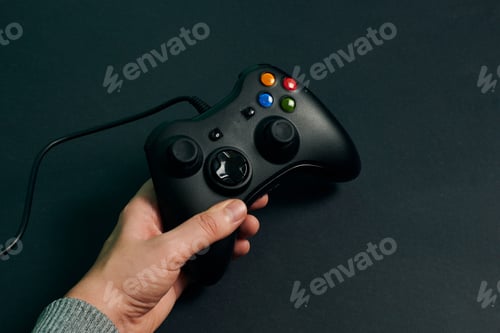 Preview: Hand of a man holding a video console controller on a black background