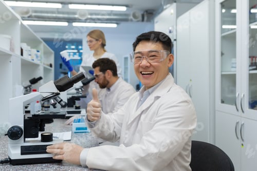 Preview: Portrait of a smiling and a young Asian male doctor, scientist sitting behind a microscope and