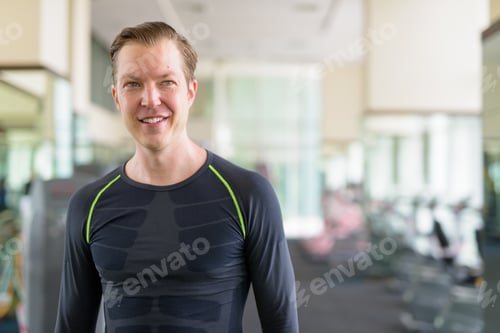 Preview: Portrait of happy young handsome man thinking at the gym during covid-19