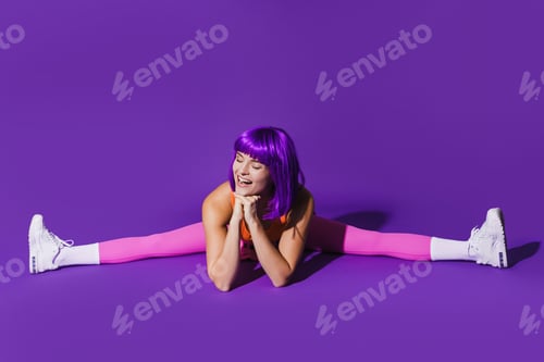 Preview: Cheerful woman wearing colorful sportswear doing splits against purple background