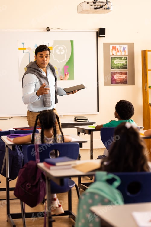 Preview: Diverse male teacher using tablet teaching with children at desks in elementary school class