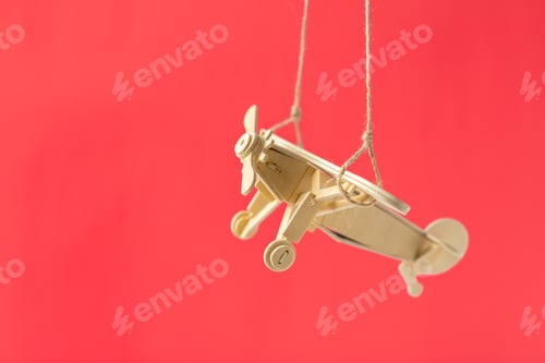 Preview: Wooden toy airplane hangs against a bright red background for playful decoration