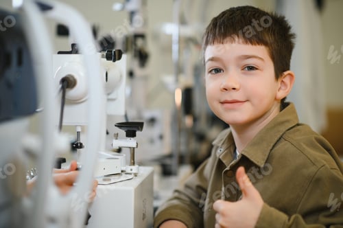 Preview: Boy showing thumb up during eye exam at ophthalmology clinic