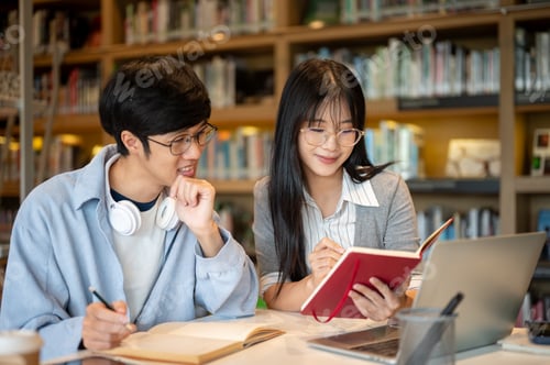Preview: Glasses asian man student smiling looking at book holding in woman friend's hand at table in library