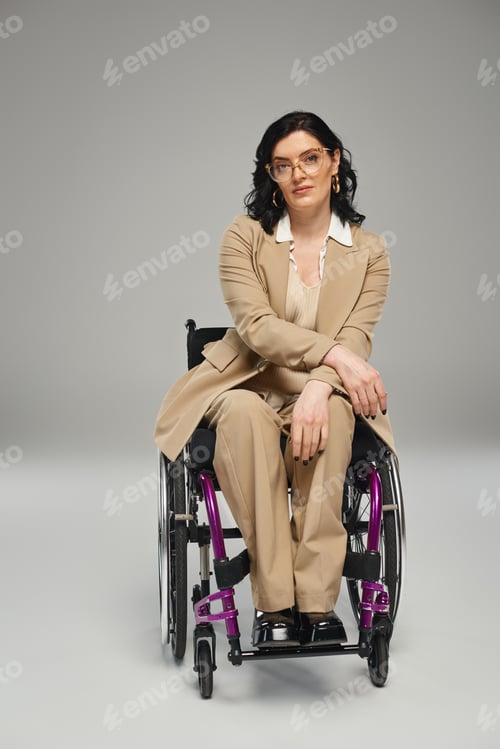 Preview: beautiful disabled woman with wavy hair in pastel suit with glasses in wheelchair looking at camera