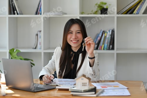 Preview: Real estate agent holding house key in hand and smiling at camera.