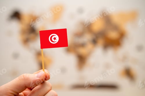 Preview: Tunisia flag in mans hand on the world map background.