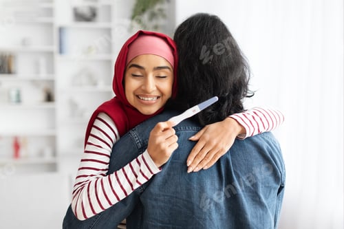 Preview: Happy Excited Young Muslim Woman Holding Positive Pregnancy Test And Hugging Husband
