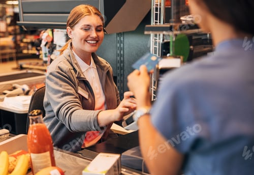 Preview: Smiling cashier in a grocery store receiving payment from a customer