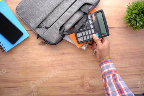 Preview: top view of young man putting office stationary in his bag