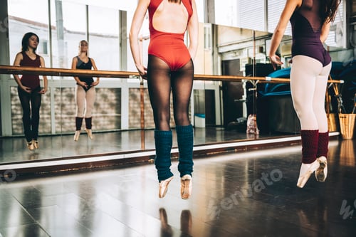 Preview: Crop women in bodysuits jumping on pointe above floor in studio training ballet.