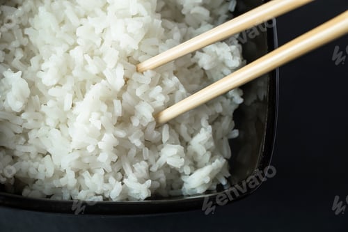 Preview: Bowl with boiled rice on black background. Asian food and bamboo chopsticks.