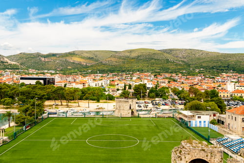 Preview: Elevated view of a football stadium with a town and mountains in the background