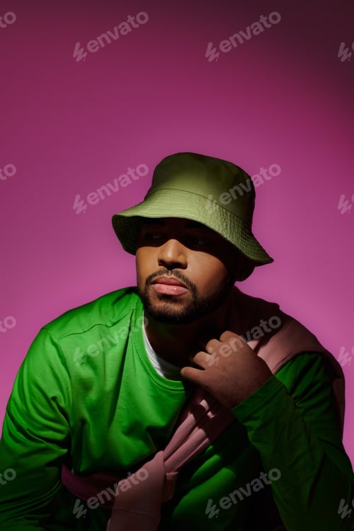 Preview: handsome bearded man in green panama with sweatshirt tied on his shoulders, fashion concept