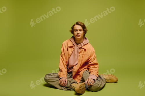Preview: Young man showcases vibrant fashion style against a bold green backdrop in a modern setting