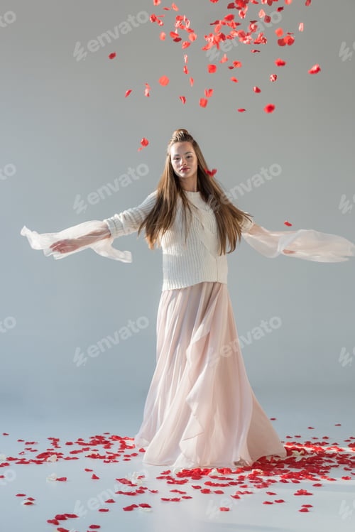 Preview: attractive woman in fashionable winter outfit spinning around under falling red roses petals