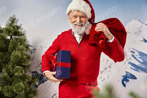 Preview: cheerful man in Santa costume holding present bag and big gift looking at camera, winter concept