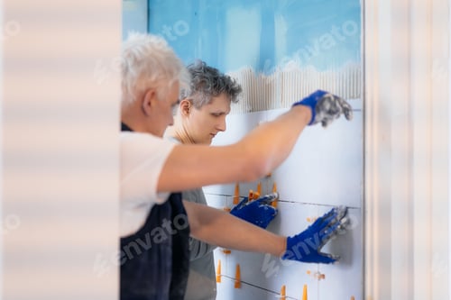 Preview: Father and son laying tiles on a bathroom wall. DIY concept. House improvement