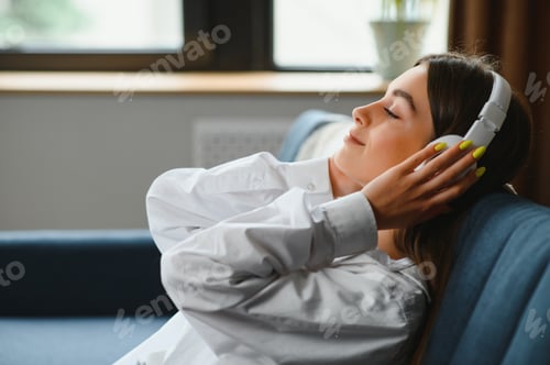 Preview: Beautiful young caucasian woman in casual clothing enjoying music and smiling while resting at home.