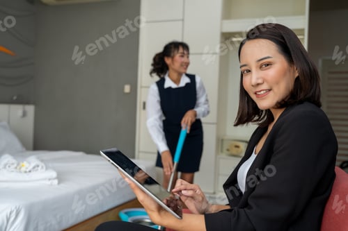 Preview: Housekeeping manager working on digital tablet and controlling the work of staff in the hotel room.