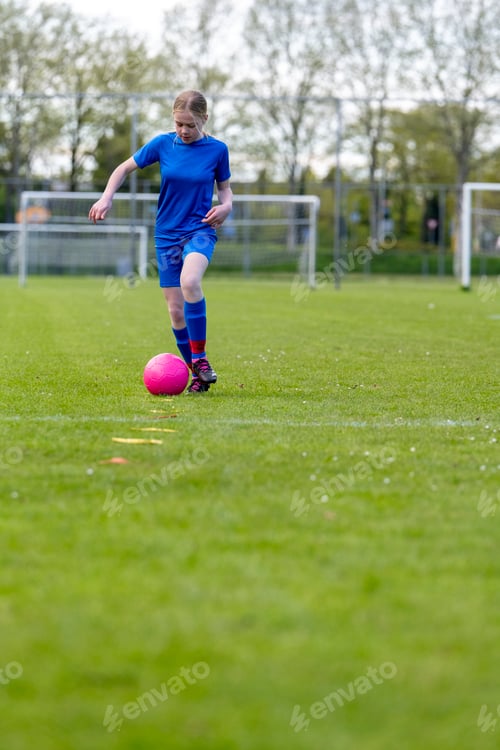 Preview: Young girl in blue sports attire playing soccer on a grassy field with a pink ball.