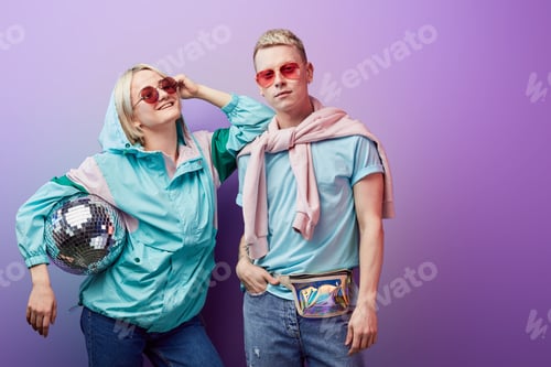 Preview: Young fashionable couple of dancers posing with disco ball on violet background