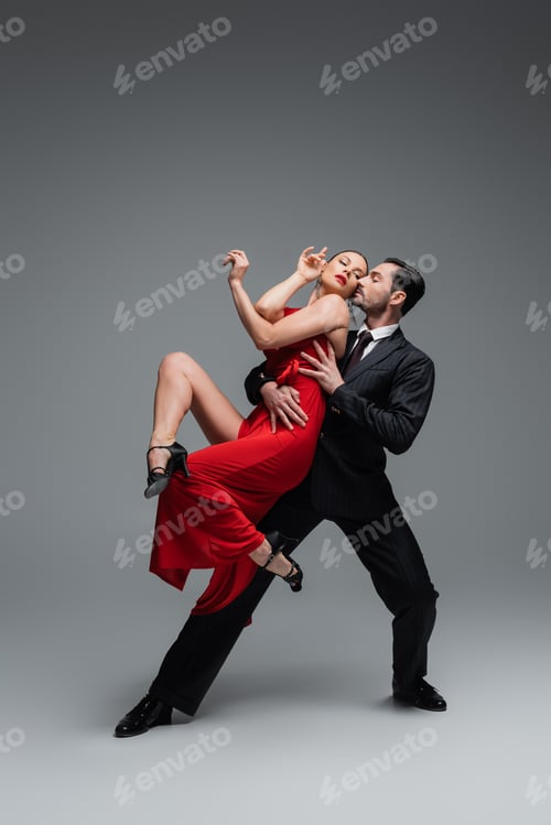 Preview: Full length of stylish couple performing tango on grey background
